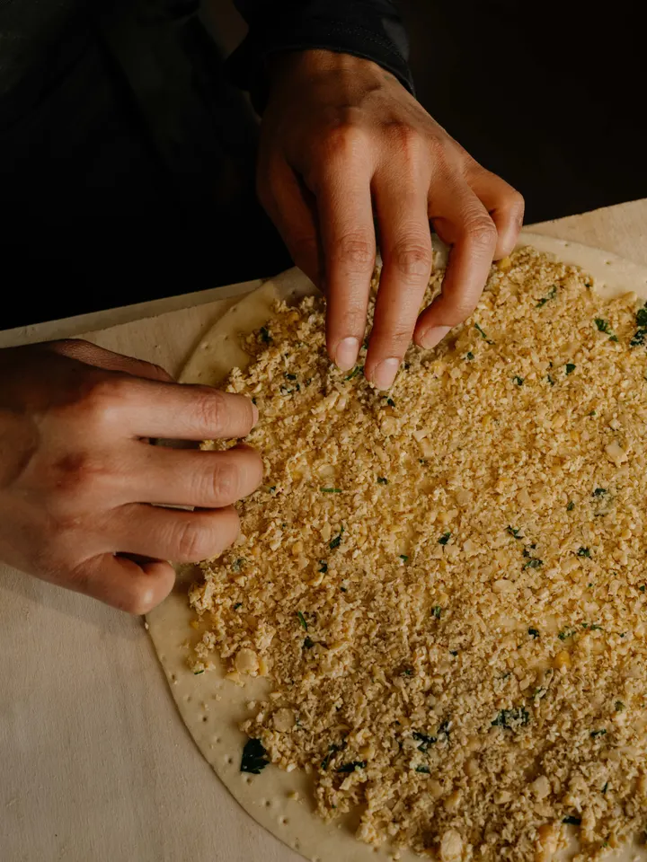 Due mani che distribuiscono lo zaatar su un disco di impasto